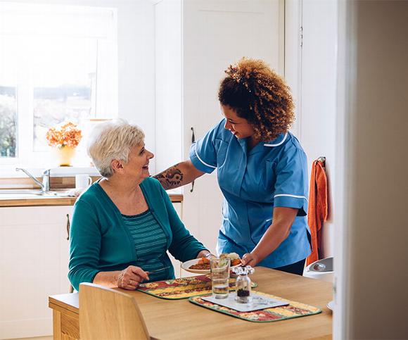 Carer Giving dinner to older lady in Kitchen
